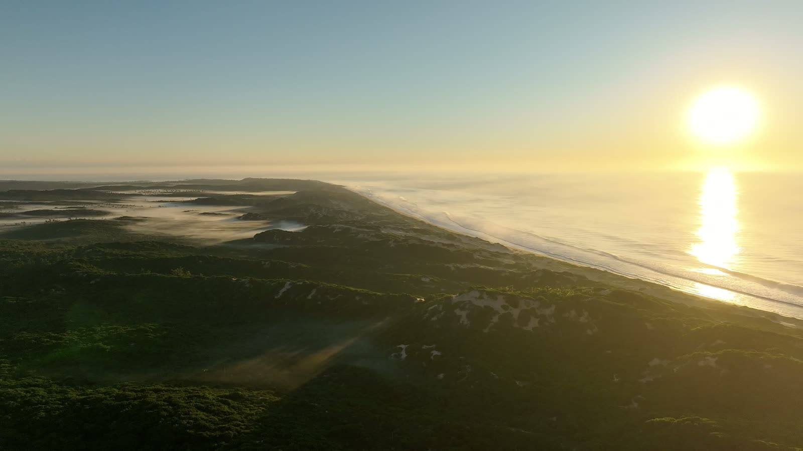 Aerial film of sunrise over the green dunes and Indian Ocean at Reserva Dunas Verdes